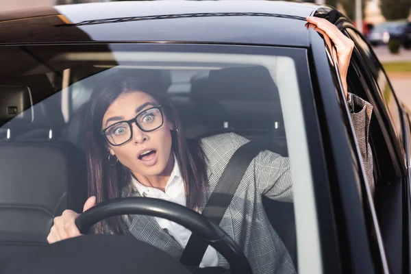 Шокована бізнес-леді дивиться далеко під час водіння автомобіля на розмитому передньому плані — стокове фото