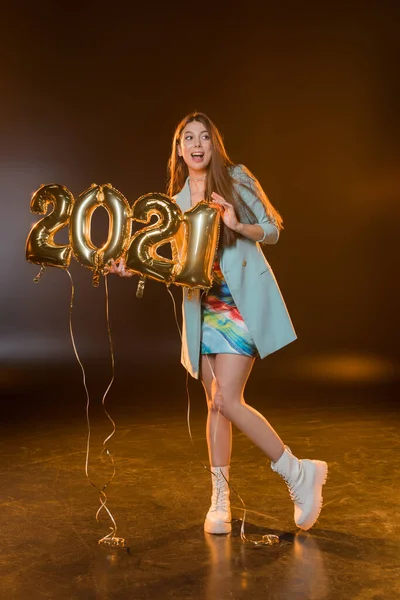 Повна довжина збудженої жінки, яка посміхається і тримає кульки 2021 року на чорному — стокове фото