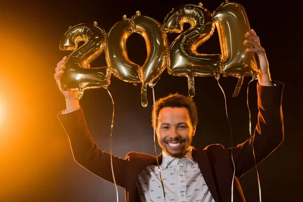 Joyeux homme afro-américain tenant 2021 numéros ballons au-dessus de la tête sur noir — Photo de stock