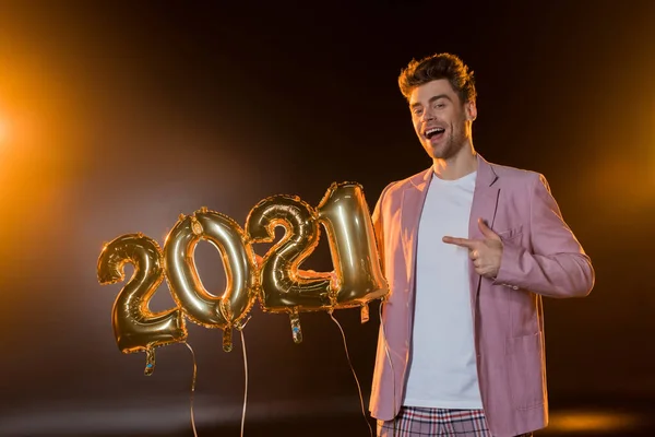 Alegre hombre apuntando con el dedo a 2021 números globos en negro - foto de stock