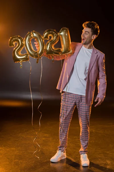Full length of cheerful man holding 2021 numbers balloons on black — Stock Photo