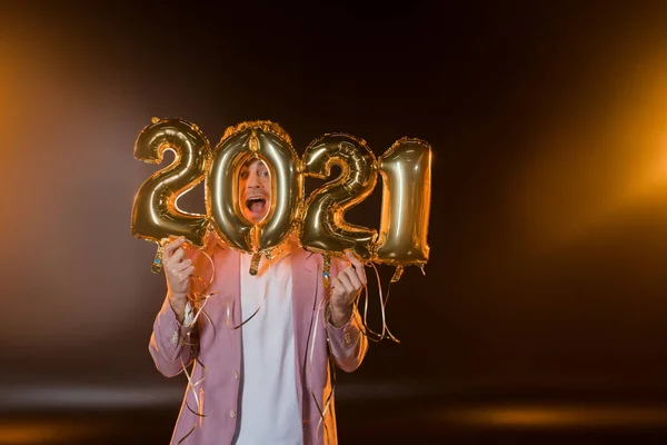 Excité homme se cachant derrière 2021 numéros ballons sur noir — Photo de stock