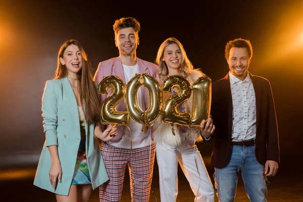 Group of happy multicultural friends holding 2021 numbers balloons on black — Stock Photo