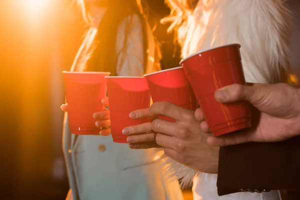 Cropped view of friends toasting plastic cups on black — Stock Photo