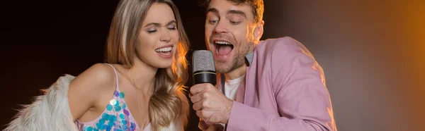 Man and blonde woman singing while holding microphone on black, banner — Stock Photo