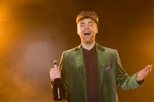 Hombre feliz en blazer verde y corona sosteniendo botella de champán en negro - foto de stock