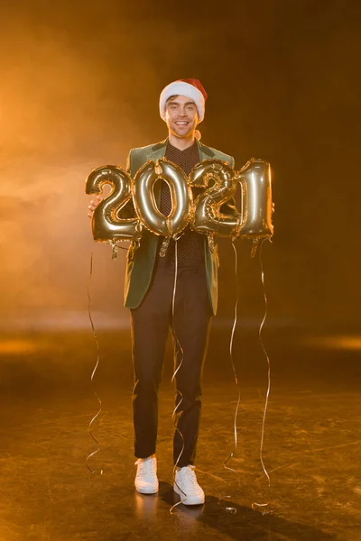 Longitud completa de hombre feliz en el sombrero de santa celebración de globos con 2021 números en negro - foto de stock