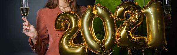 Partial view of couple holding balloons with 2021 numbers and glasses of champagne on black — Stock Photo