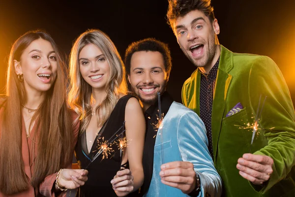 Felizes amigos multiculturais segurando faíscas em chamas no preto — Fotografia de Stock