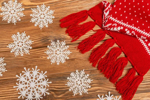 Top view of winter snowflakes and red knitted scarf on wooden background — Stock Photo