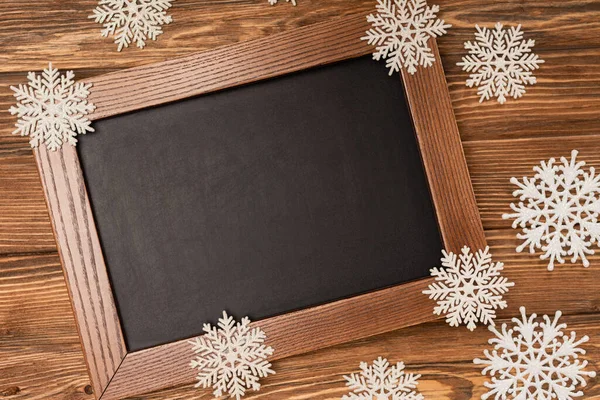 Top view of winter snowflakes on chalkboard on wooden background — Stock Photo