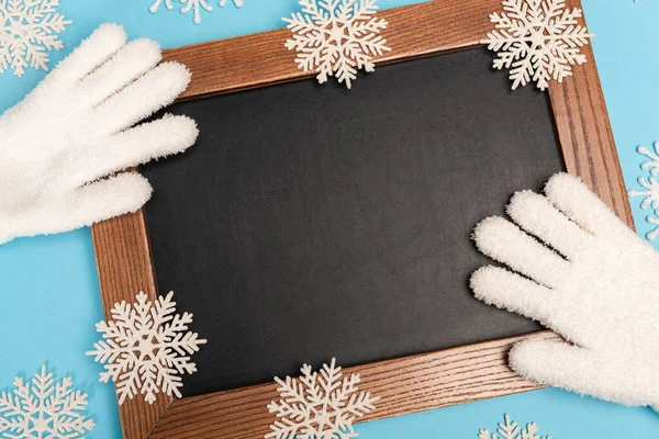 Blick von oben auf weiße Winterhandschuhe, Kreide und Schneeflocken auf blauem Hintergrund — Stockfoto