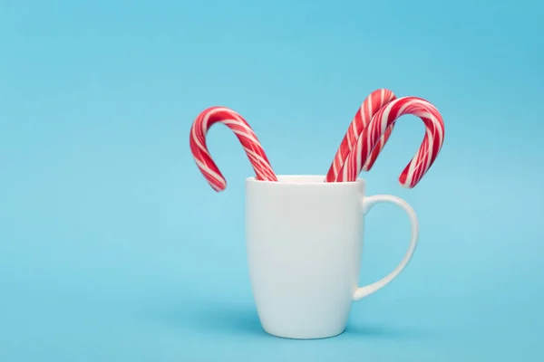Candy canes in white mug on blue background — Stock Photo
