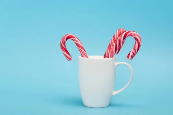 Bastones de caramelo en taza blanca sobre fondo azul - foto de stock