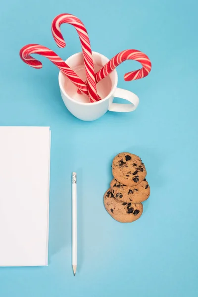 Top view of chocolate cookies, candy canes and blank notebook on blue background — Stock Photo