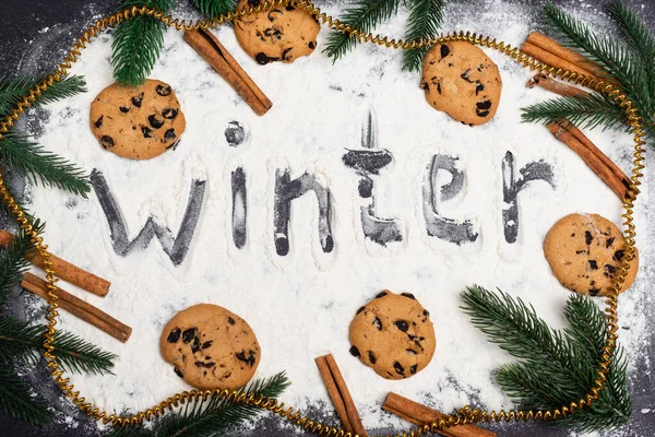 Top view of word winter, fir branches and chocolate cookies on black background — Stock Photo