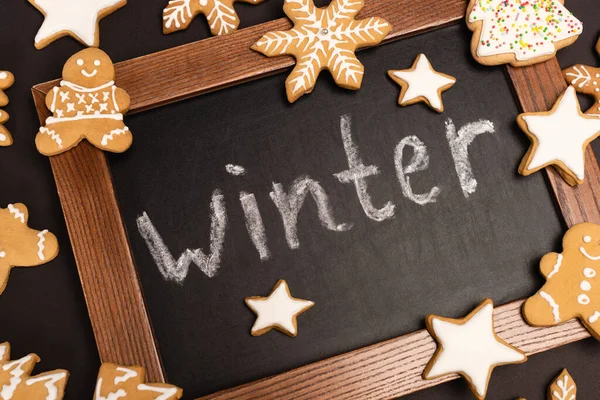 Top view of gingerbread cookies and word winter on chalkboard on black background — Stock Photo