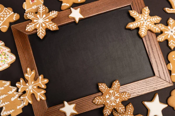Top view of gingerbread cookies and chalkboard on black background — Stock Photo