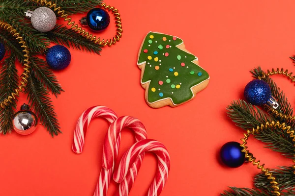 Вид зверху на прикрашену ялинку, печиво та цукерки на червоному тлі — стокове фото