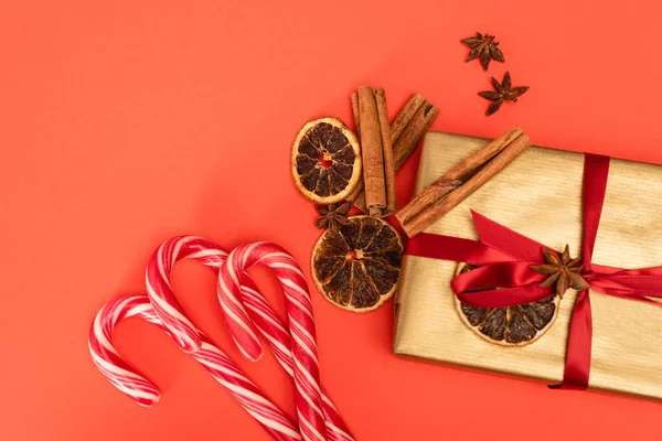 Top view of gift with spices and candy canes on red background — Stock Photo