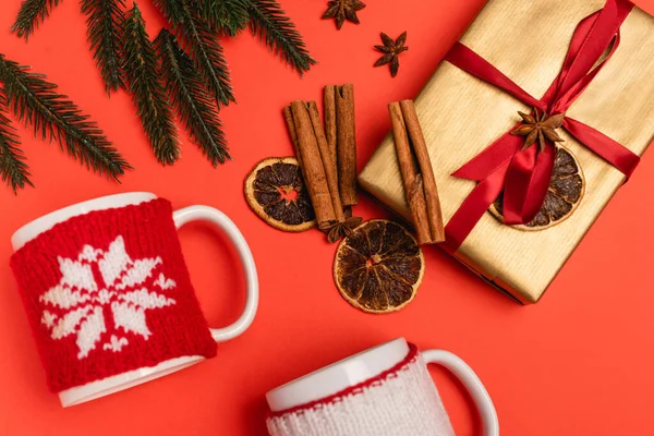 Vue du dessus de l'arbre de Noël, cadeau avec des épices et des tasses sur fond rouge — Photo de stock