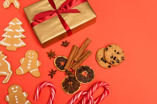 Vista superior de regalo, bastones de caramelo, especias y galletas de jengibre sobre fondo rojo - foto de stock