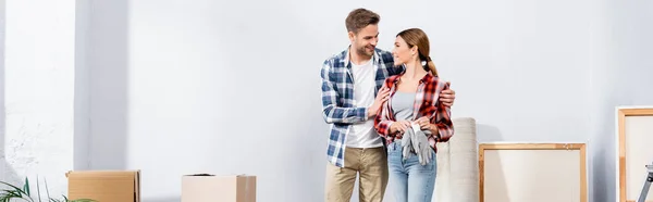 Feliz joven abrazando y mirando a la novia con guantes en casa, pancarta - foto de stock