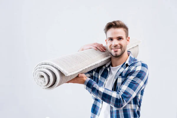Glücklicher junger Mann mit Teppichrolle blickt isoliert auf weiße Kamera — Stockfoto