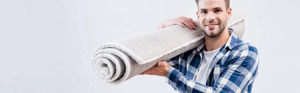 Happy young man looking at camera while holding carpet roll isolated on white, banner — Stock Photo