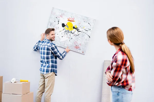 Lächelnder junger Mann, der die Frau ansieht, während er das Bild zu Hause auf verschwommenem Vordergrund entfernt — Stockfoto