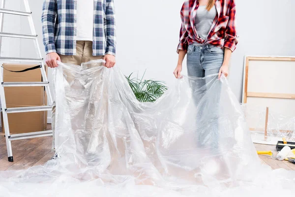 Cropped view of young couple holding polyethylene near ladder at home — Stock Photo