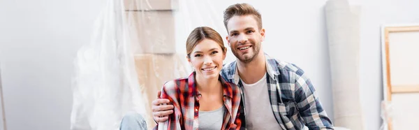 Smiling young couple looking at camera during repair at home on blurred background, banner — Stock Photo