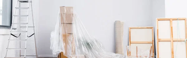 Intérieur de la chambre avec échelle, photos, rouleau de tapis et boîtes en carton recouvert de polyéthylène, bannière — Photo de stock