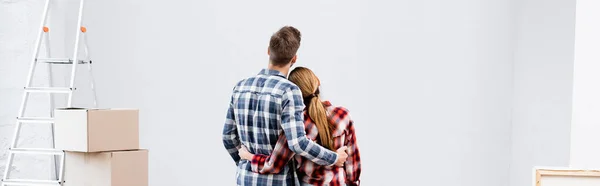 Вид на молодую пару, обнимающуюся возле лестницы и картонных коробок дома, баннер — стоковое фото