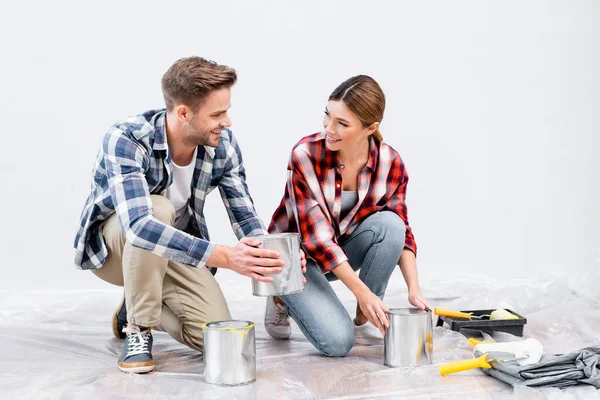 In voller Länge glückliches junges Paar, das sich gegenseitig ansieht, während es zu Hause auf dem Boden in der Nähe von Farbdosen sitzt — Stockfoto