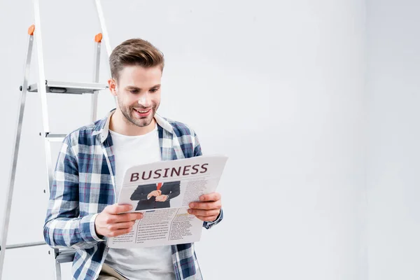 Счастливый молодой человек читает газету с деловыми надписями возле лестницы в помещении — стоковое фото