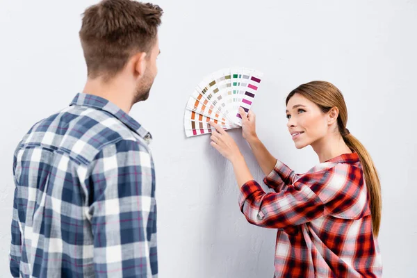 Mujer joven sonriente mirando al hombre mientras señala con el dedo la paleta de colores en el interior - foto de stock