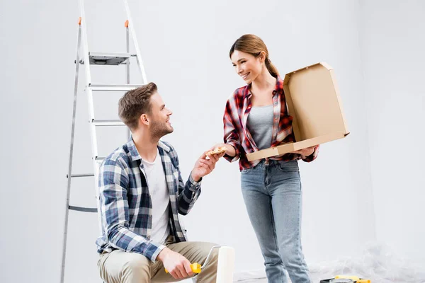 Glücklicher junger Mann nimmt Frau bei Leiter zu Hause ein Stück Pizza weg — Stockfoto