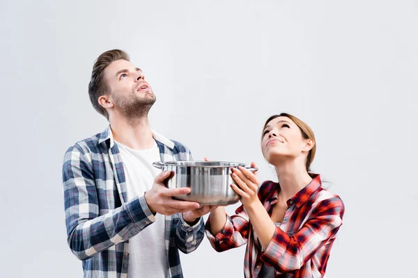 Pareja joven mirando hacia arriba mientras sostiene la olla bajo el techo con fugas - foto de stock