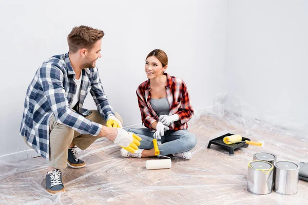 In voller Länge glückliches junges Paar in Handschuhen, das sich gegenseitig ansieht, während es zu Hause auf dem Boden sitzt — Stockfoto