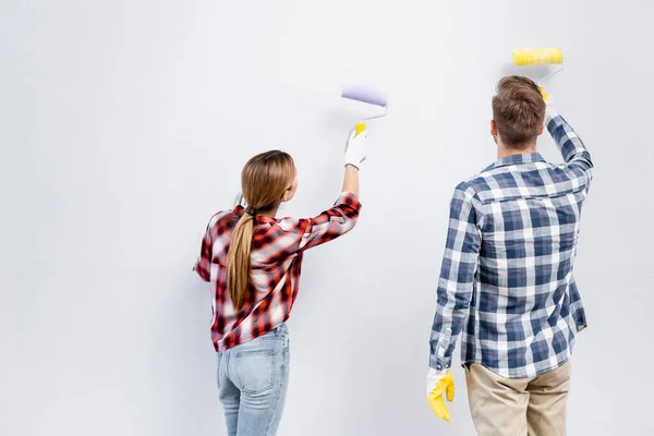 Visão traseira do jovem casal com rolos de parede de pintura em casa — Fotografia de Stock