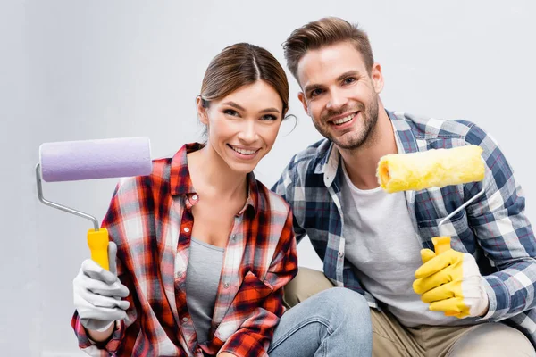 Heureux jeune couple regardant caméra tout en tenant rouleaux de peinture — Photo de stock