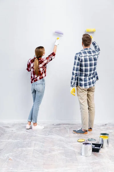 Vue arrière du jeune couple avec des rouleaux mur de peinture à la maison — Photo de stock