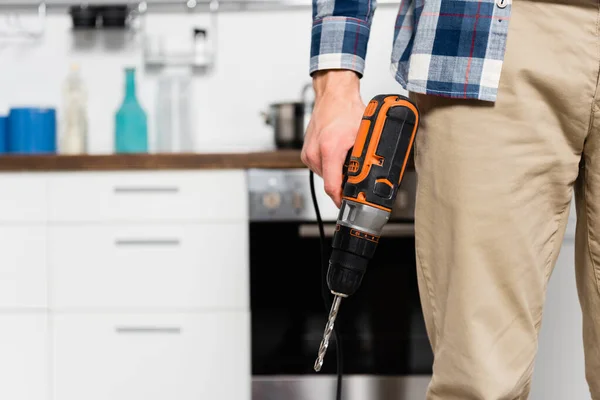 Cropped view of young man holding drill with blurred kitchen on background — Stock Photo