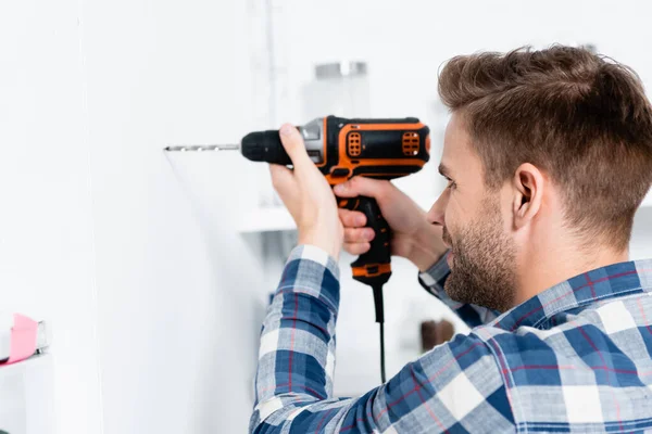 Junger glücklicher Mann bohrt Wand auf verschwommenem Hintergrund in Küche — Stockfoto