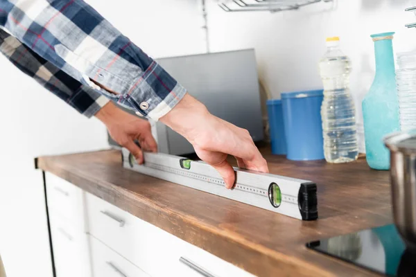 Cropped view of young man holding measuring level tool on table in kitchen on blurred background — Stock Photo