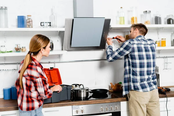 Giovane donna guardando l'uomo con cacciavite che ripara ventilatore estrattore in cucina — Foto stock