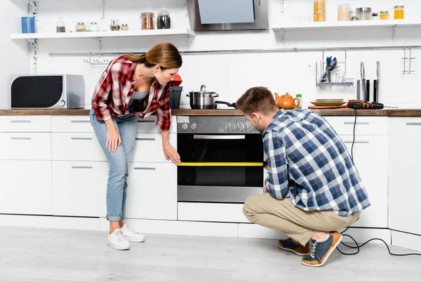 Comprimento total do jovem casal com fita métrica forno na cozinha — Fotografia de Stock
