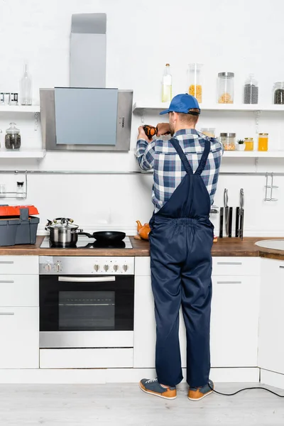 Back view of handyman with drill repairing shelves in kitchen — Stock Photo