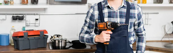 Cropped view of handyman holding drill on blurred background in kitchen, banner — Stock Photo